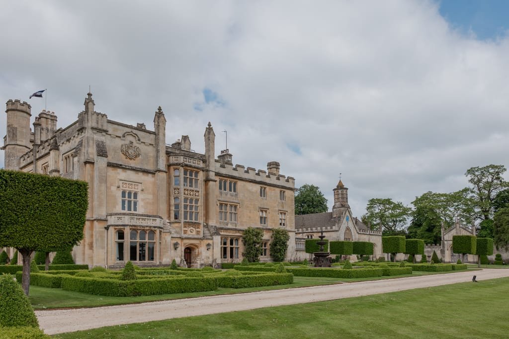 A large stone manor with groomed hedges, a gravel pathway, and a clear sky—an idyllic setting for a Farleigh House Wedding Photographer to capture timeless moments.
