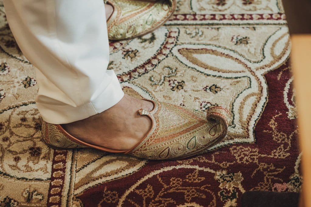 A person wearing white pants and ornate, pointed shoes stands on a patterned rug, evoking wedding traditions from around the world.