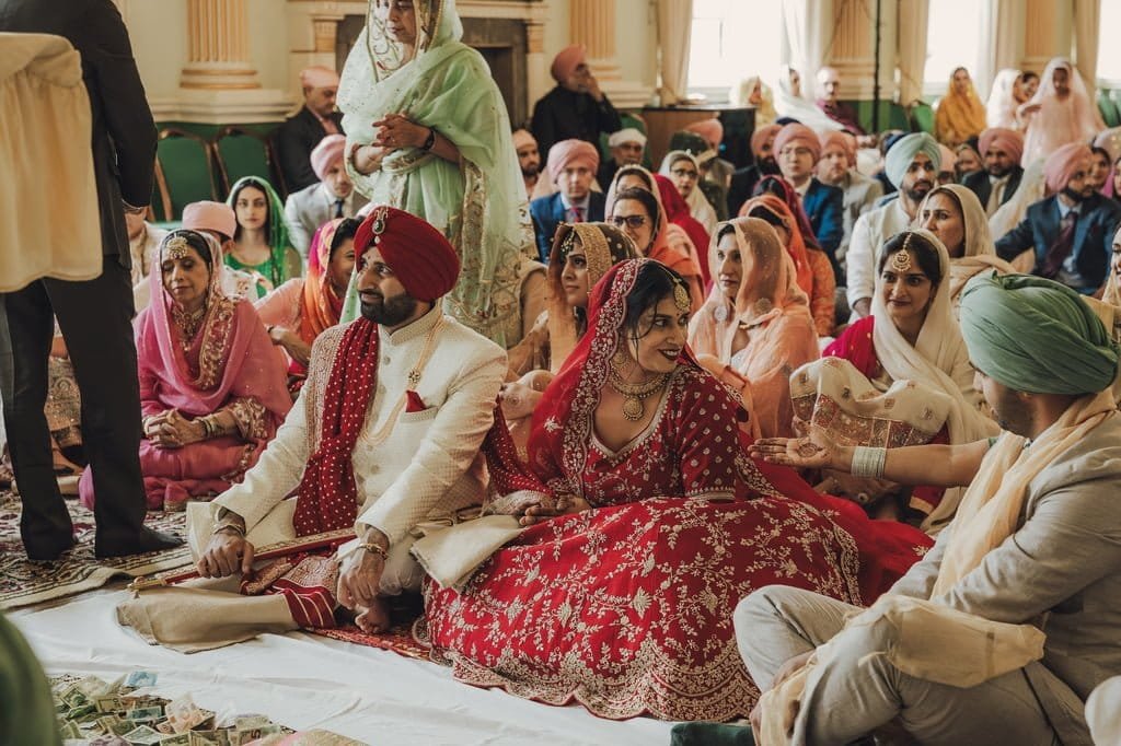 Bride and groom in traditional attire sit among guests during a wedding ceremony, surrounded by family and friends, embracing wedding traditions from around the world.