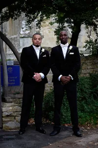 Two men in black suits posing for a picture, captured by a wedding photographer.
