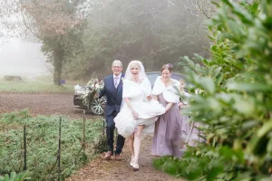 A bride and her bridesmaids walking down a path in the Orchardleigh House Photos, enveloped by the ethereal fog.