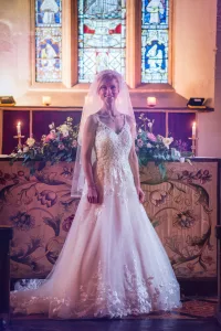 A bride in a wedding dress standing in front of a stained glass window at Orchardleigh House.