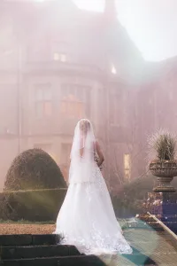 A bride is standing on the steps of Orchardleigh House for her wedding photos.