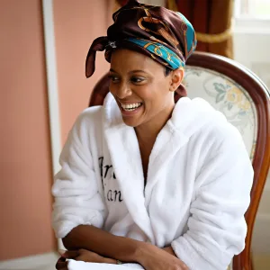 A woman in a white bathrobe smiling while sitting in a chair.