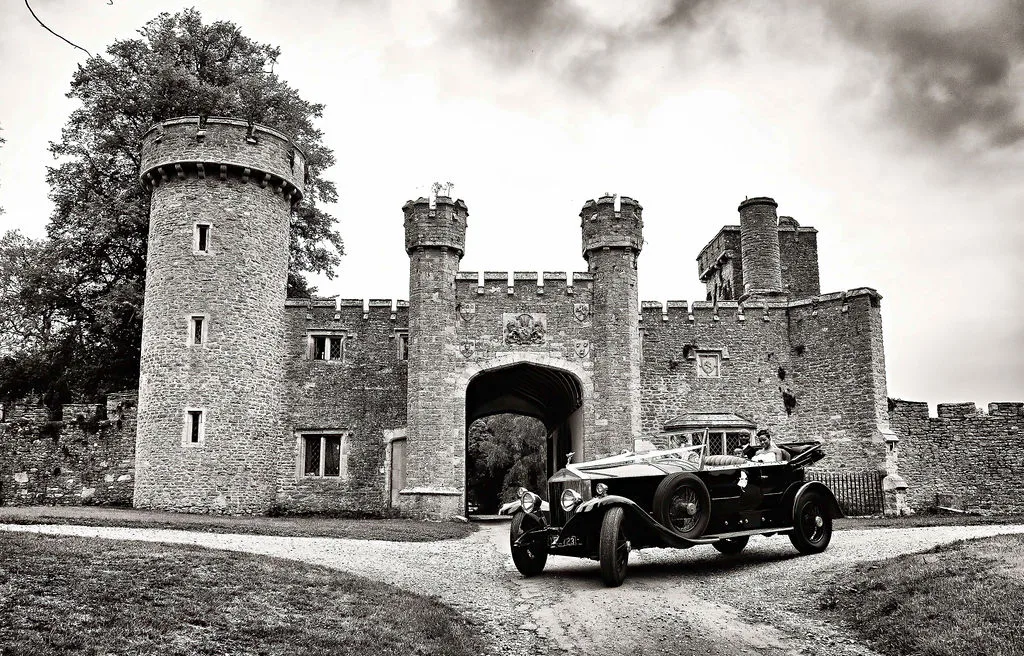 A black and white photo of an old car in front of a castle, captured by Orchardleigh Wedding Photography.