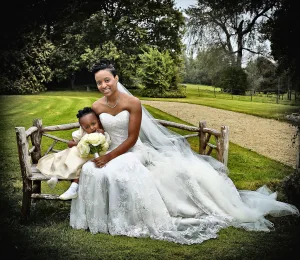 A woman in a wedding dress and a little girl sitting on a bench at Orchardleigh Wedding Photography.