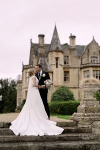 Castle Combe Manor wedding photographer captures a bride and groom standing in front of the grand mansion.