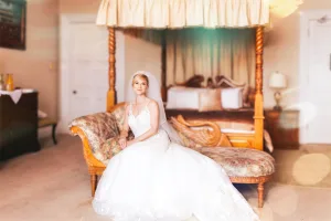 A bride sitting on a bed in Orchardleigh House, surrounded by the elegance of a four poster bed.