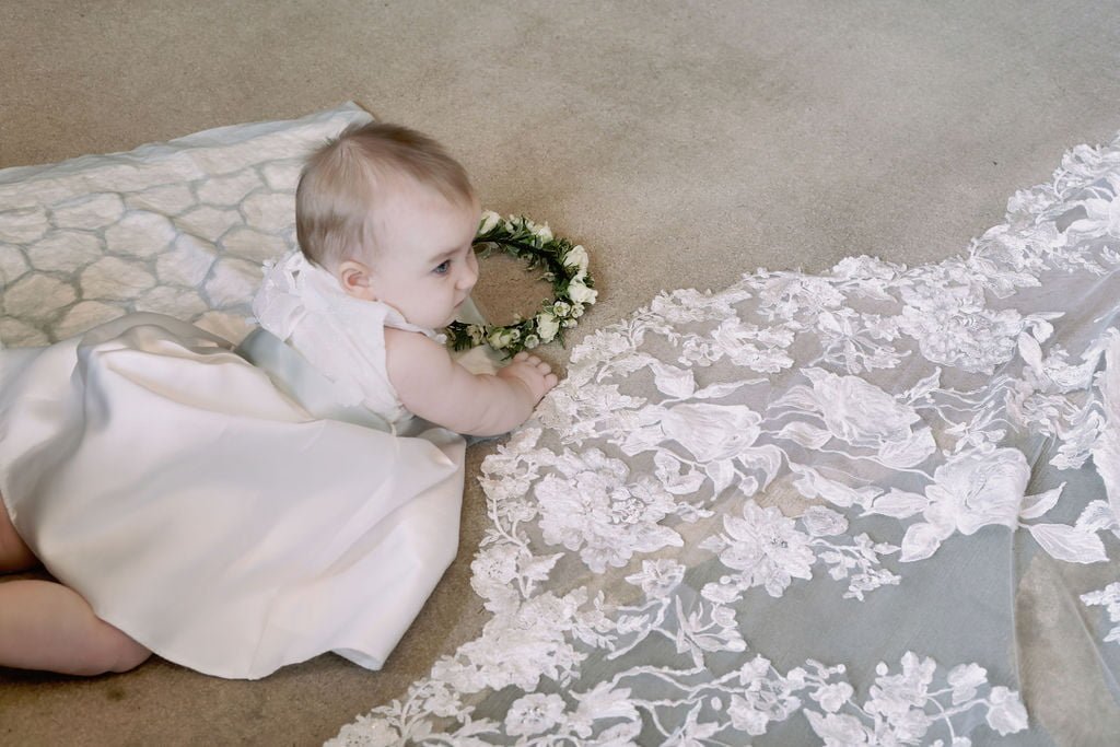 a baby in a white dress sitting on the floor.