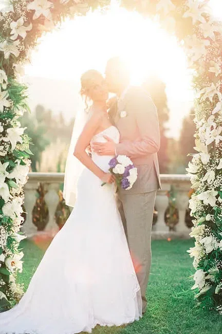 a bride and groom standing under a floral arch.