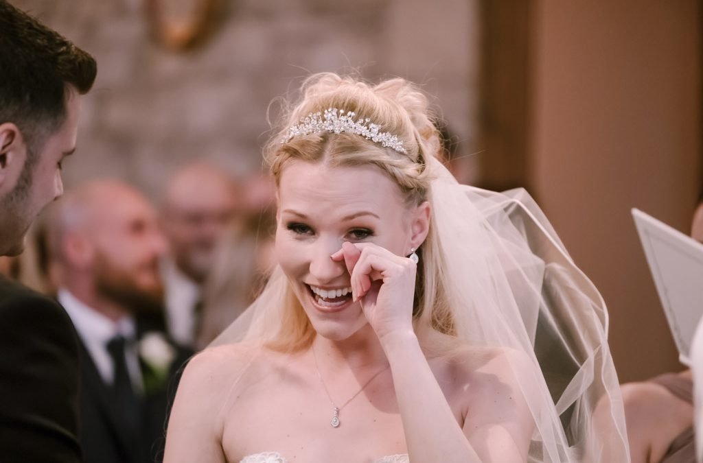 a woman in a wedding dress smiles as she holds her hand to her face.