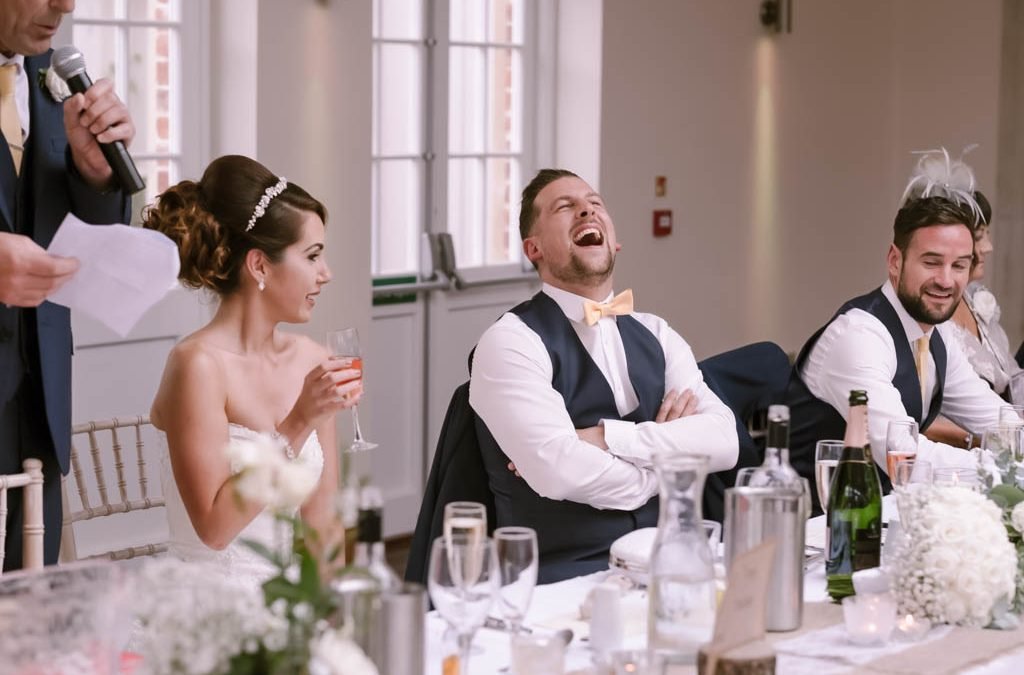 A bride and groom sharing joyful laughter during their Orchardleigh wedding speech, captured beautifully by a skilled wedding photographer.