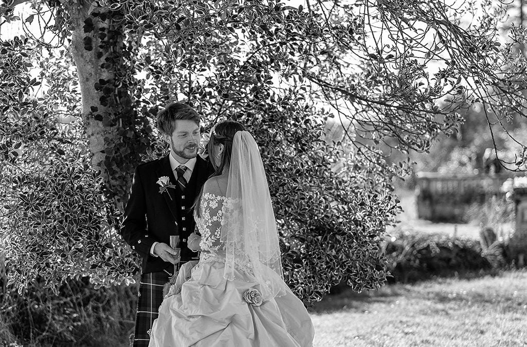 a bride and groom pose for a picture under a tree.