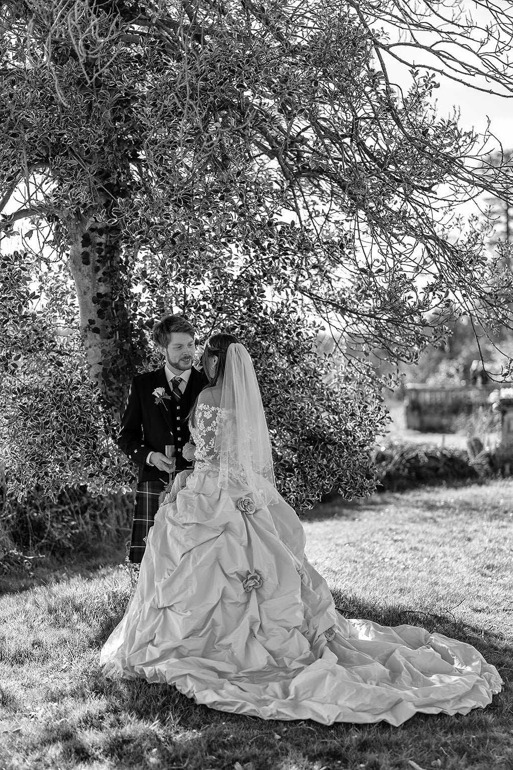 a bride and groom pose for a picture under a tree.
