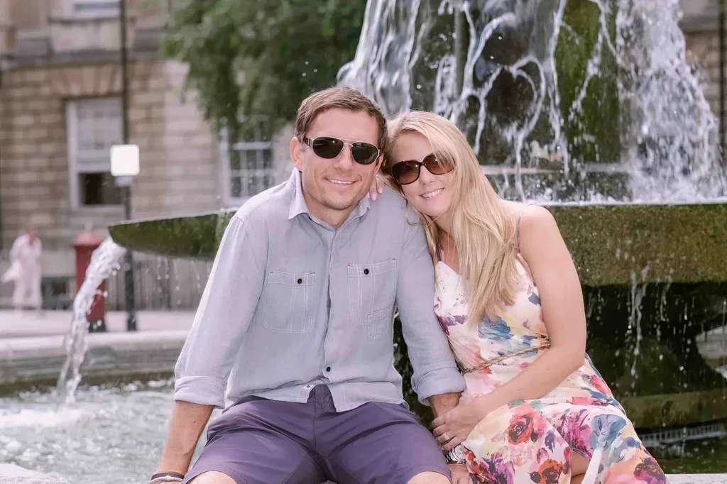 Say Cheese:a man and a woman sitting on a bench in front of a fountain.