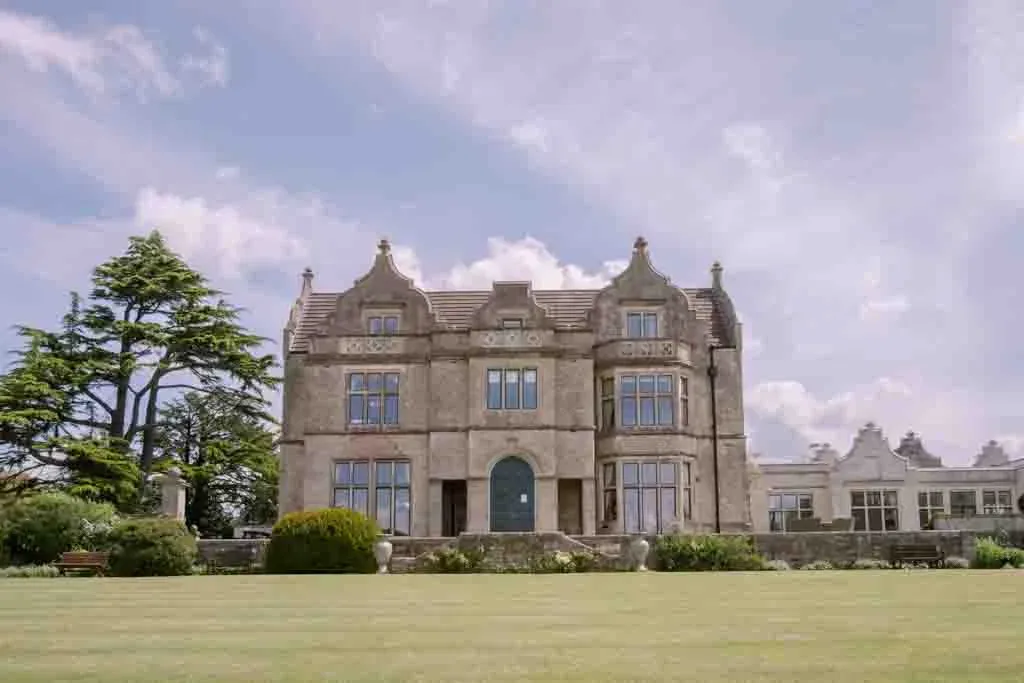 a large stone building with a green lawn in front of it Old Down Manor