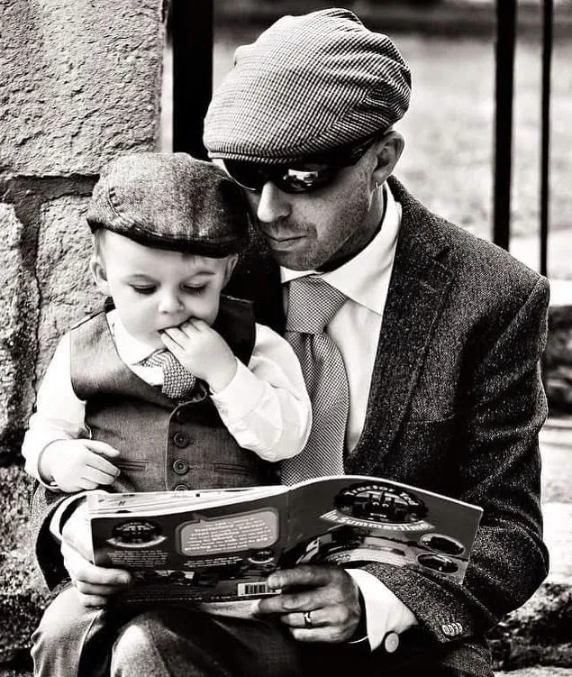 a man holding a small child while reading a book.