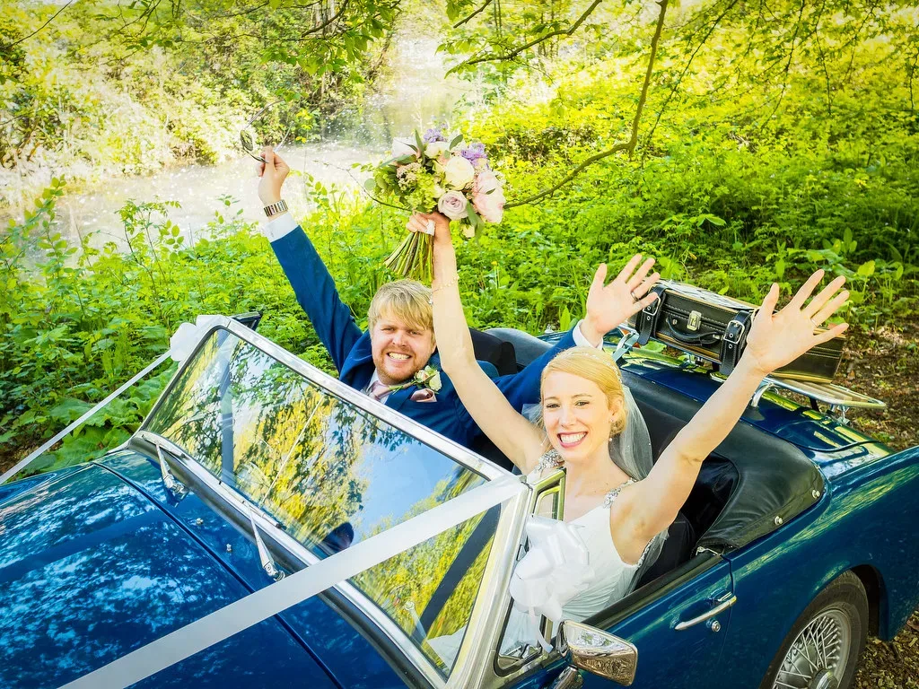 Hitch a ride :a bride and groom sitting in a blue convertible car.