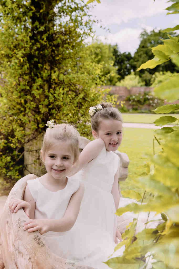 two little girls in white dresses sitting on a bench.