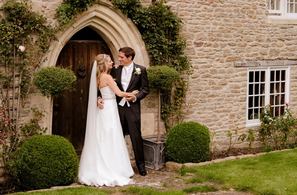 Guide to hiring a wedding Photographer: Wick farm Weddings: a bride and groom standing in front of a stone building.