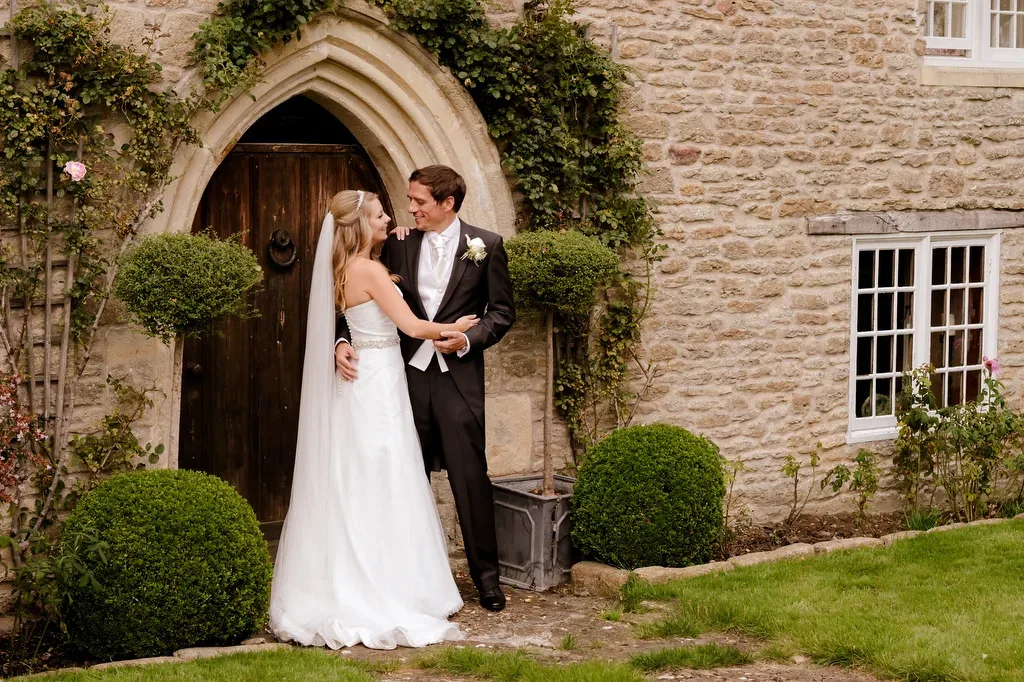 Guide to hiring a wedding Photographer: Wick farm Weddings: a bride and groom standing in front of a stone building.