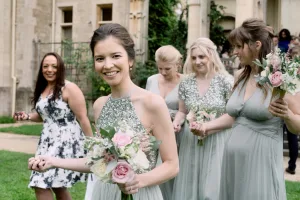 The Manor Castle Combe Wedding Photographer captures a bride and her bridesmaids elegantly walking in front of a stunning building on their special day.