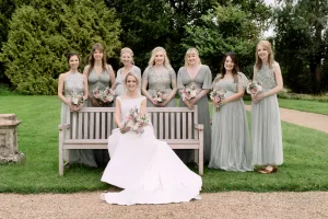 A bride, along with her bridesmaids, poses on a bench at The Manor Castle Combe.