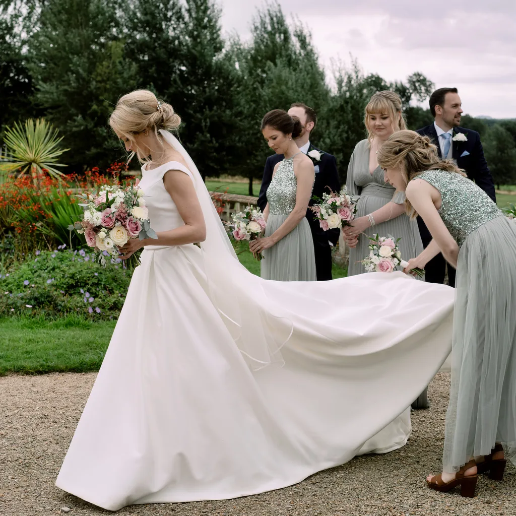 A bride is being helped by her bridesmaids during a picturesque Castle Combe Manor wedding, beautifully captured by the wedding photographer.