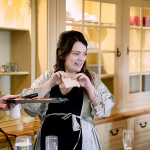A woman is holding a tray of food in a kitchen at Castle Combe Manor.