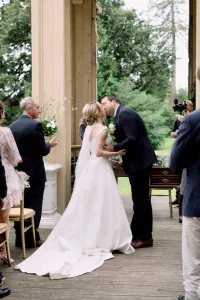 A couple celebrates their special day as Castle Combe Manor Wedding Photographer captures their kiss amidst a crowd of people.
