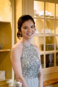 A woman in a silver dress smiling in front of Castle Combe Manor kitchen.