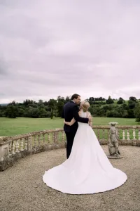 A bride and groom embracing on a balcony overlooking Castle Combe Manor, captured by a skilled wedding photographer.