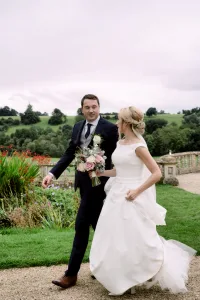 A bride and groom walking down a path in a garden captured by a Castle Combe Manor wedding photographer.