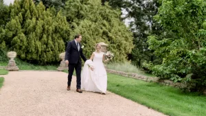 A bride and groom strolling through the picturesque garden of Castle Combe Manor on their wedding day.