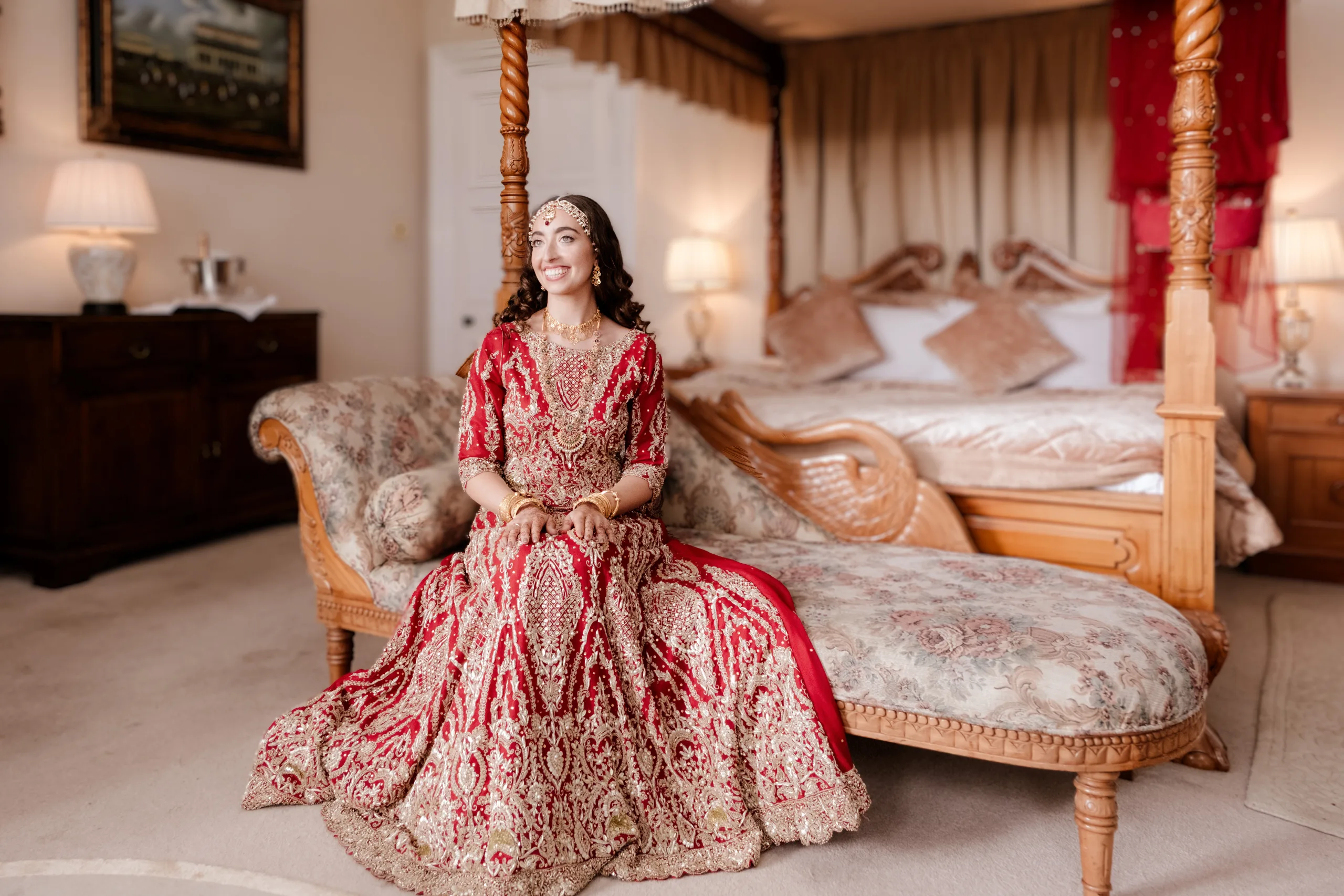 A bride in a red dress sitting on a bed in a bedroom. Wick farm Weddimngs