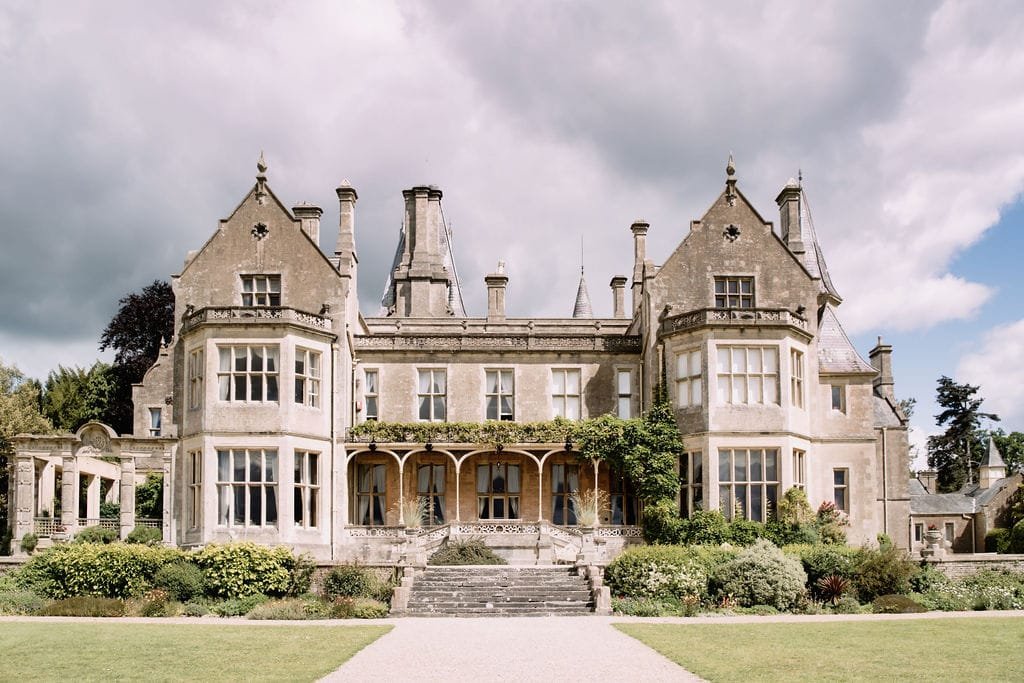 Nestled in a lush garden, this historic stone manor with ornate gables and chimneys provides the perfect backdrop for Elmhay Park wedding photography, its timeless elegance accentuated by the dramatic cloudy sky.