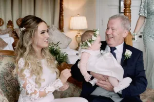 An Orchardleigh House wedding photographer capturing a joyful moment of a bride and groom with their beloved baby sitting on a bed.