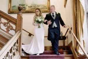 A bride and her father gracefully descend the stairs at Orchardleigh House, captured by a talented wedding photographer.