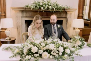 Orchardleigh House Wedding Photographer captures a charming scene of a bride and groom sitting at a table adorned with flowers.