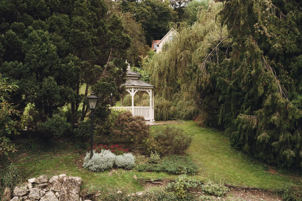 A white gazebo sits in the middle of a wooded area. Limply Stoke Hotel Weddings