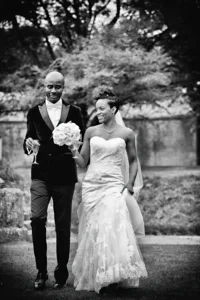 A newlywed couple walking hand-in-hand at Orchardleigh House, the bride holding a bouquet and the groom in a black suit.