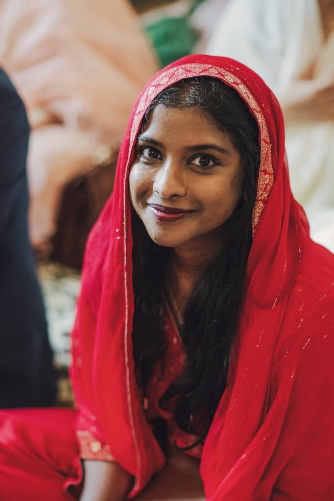 A woman in a red traditional outfit and headscarf, embodying wedding traditions from around the world, smiles at the camera.