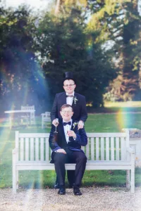 _DSF7805 Orchardleigh Wedding Photography captures the elegant essence of two men in tuxedos as they confidently sit on a bench.