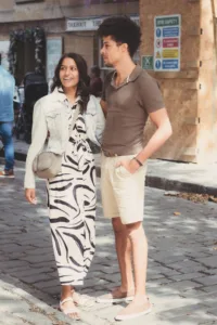 A woman in a zebra print dress and a man in a brown t-shirt and beige shorts walking together on a sunny street during their complimentary engagement photo shoot.