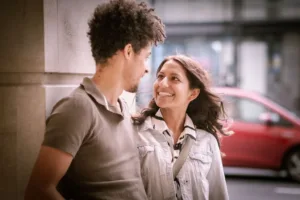 Two people smiling at each other on a city street during their complimentary engagement photo shoot.