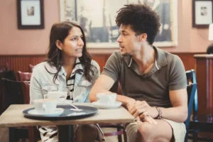 Two people having a complimentary engagement photo shoot conversation over coffee in a café.