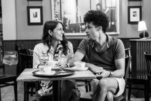 Two people engaged in a complimentary engagement photo shoot at a cafe table with coffee cups in front of them.