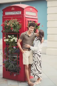 A couple posing affectionately beside a traditional red British telephone box adorned with flowers during their complimentary engagement photo shoot.
