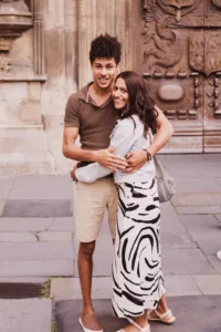 A couple embracing and smiling in front of an ornate building during their complimentary engagement photo shoot.