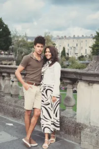 A couple posing for a complimentary engagement photo shoot with a city park in the background.